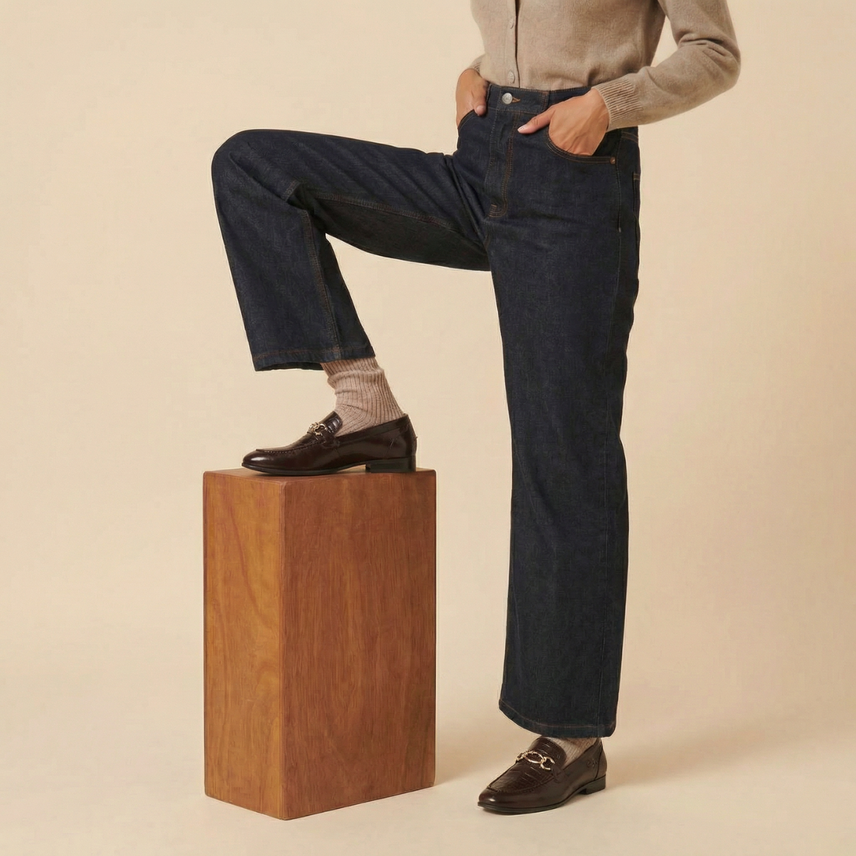 Person wearing dark blue jeans and black shoes on a beige background