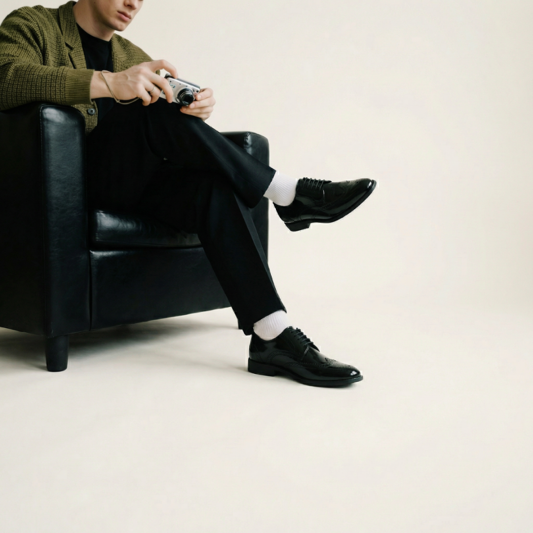 Person sitting in a black leather chair wearing black shoes and a green cardigan.
