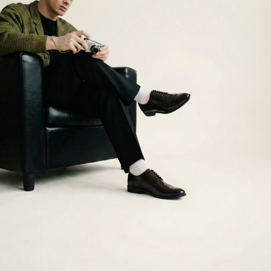 Person sitting in a black leather chair wearing brown shoes and a green cardigan.